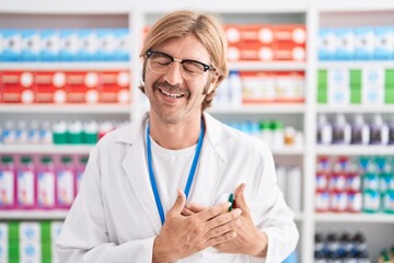 Caucasian man with mustache working at pharmacy drugstore smiling with hands on chest with closed eyes and grateful gesture on face. health concept.