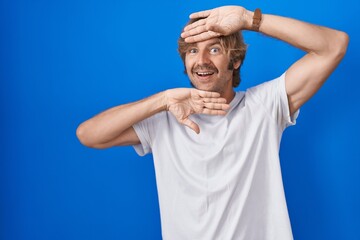 Middle age man standing over blue background smiling cheerful playing peek a boo with hands showing face. surprised and exited