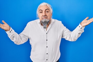 Middle age man with grey hair standing over blue background clueless and confused expression with...