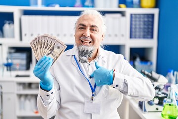 Middle age man with grey hair working at scientist laboratory holding money pointing finger to one self smiling happy and proud
