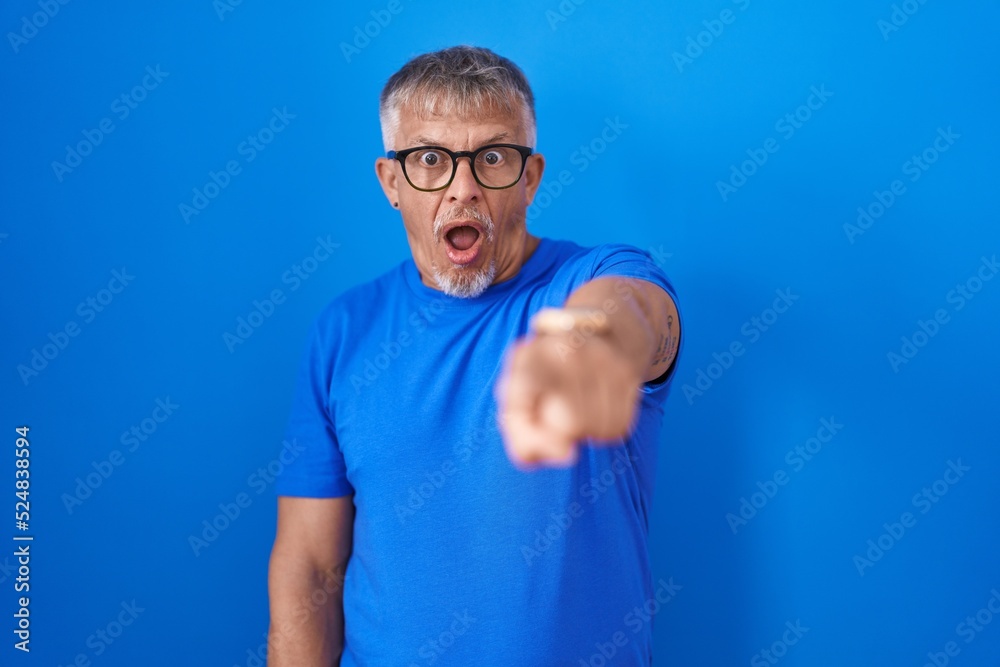 Sticker hispanic man with grey hair standing over blue background pointing displeased and frustrated to the 