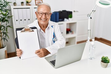Naklejka na ściany i meble Senior doctor man holding clipboard with blank space looking positive and happy standing and smiling with a confident smile showing teeth