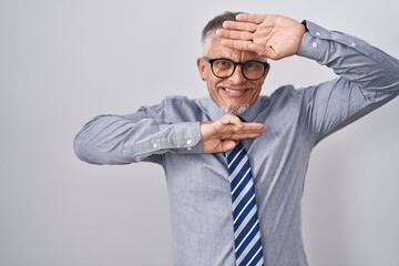 Hispanic business man with grey hair wearing glasses smiling cheerful playing peek a boo with hands showing face. surprised and exited