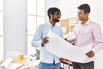 Obraz premium Two men architect workers smiling confident holding blueprint standing at architecture studio