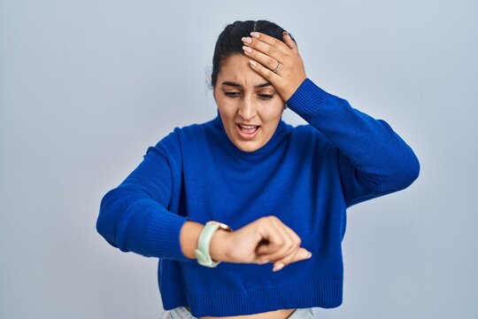 Young hispanic woman standing over isolated background looking at the watch time worried, afraid of getting late
