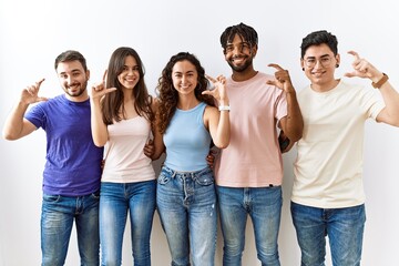 Obraz premium Group of young people standing together over isolated background smiling and confident gesturing with hand doing small size sign with fingers looking and the camera. measure concept.
