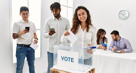 Young voter woman smiling happy putting vote in voting box at electoral center.