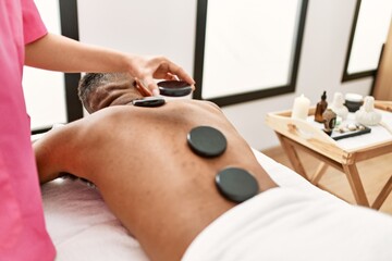 Obraz na płótnie Canvas Man reciving back massage with black stones at beauty center.