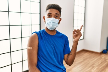 Young hispanic man with beard wearing safety mask getting vaccine smiling happy pointing with hand and finger to the side