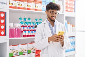 Young arab man pharmacist using smartphone standing at pharmacy
