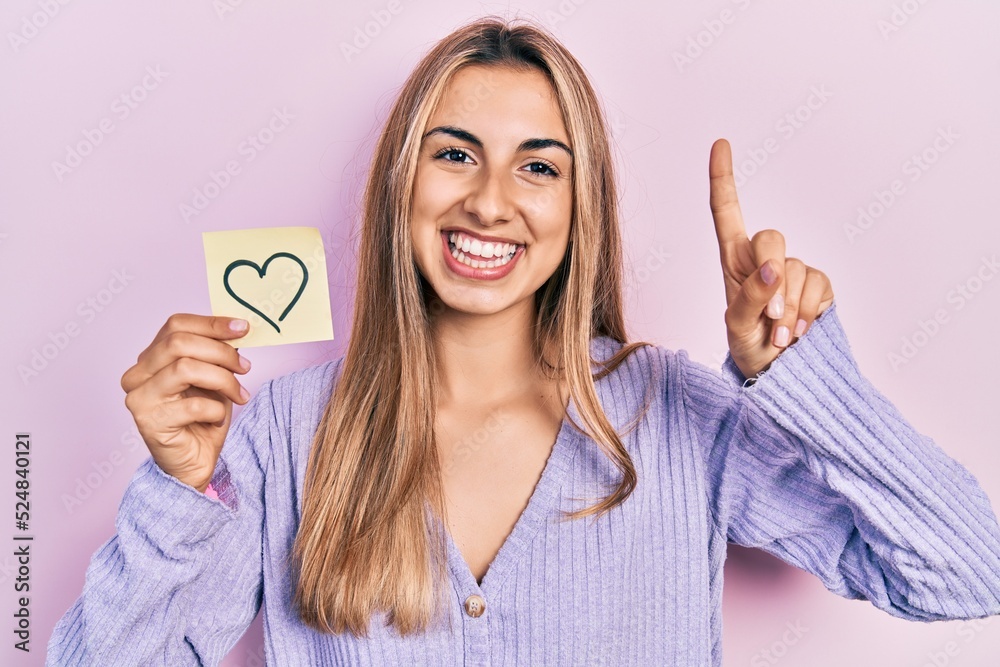 Poster beautiful hispanic woman holding heart reminder smiling with an idea or question pointing finger wit