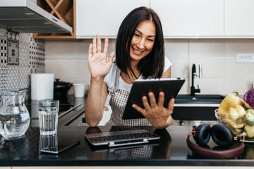 Beautiful middle age woman sitting alone in her apartment and enjoying in free time. She using laptop computer and tablet for chat and music listening.