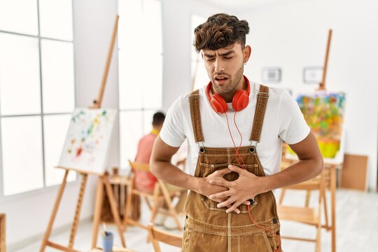 Young hispanic man at art studio with hand on stomach because indigestion, painful illness feeling unwell. ache concept.