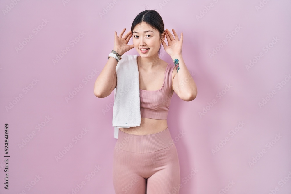 Sticker chinese young woman wearing sportswear and towel trying to hear both hands on ear gesture, curious f