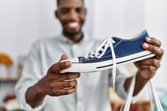 Young african american man holding shopping bag and sneaker at clothing store