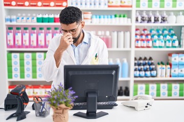 Hispanic man with beard working at pharmacy drugstore tired rubbing nose and eyes feeling fatigue and headache. stress and frustration concept. - obrazy, fototapety, plakaty