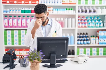 Foto op Plexiglas Hispanic man with beard working at pharmacy drugstore tired rubbing nose and eyes feeling fatigue and headache. stress and frustration concept. © Krakenimages.com