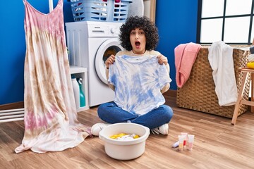 Young brunette woman with curly hair dyeing tye die t shirt and dress celebrating crazy and amazed...
