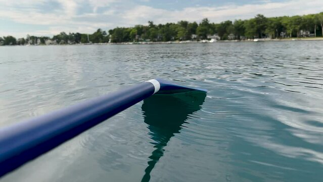 Stunning lake views from the point of view of a paddle board. Blue paddle board oar is skimming the waters surface. Views of the shoreline can be seen in the distance.