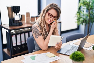 Young woman business worker talking on smartphone reading paperwork at office