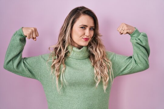Young caucasian woman standing over pink background showing arms muscles smiling proud. fitness concept.