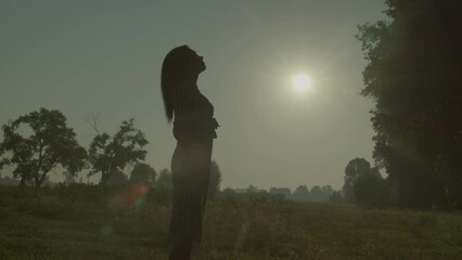 Carefree elegant attractive African American woman in summer dress whirling on field with arms outstretched, enjoying recreation, life and freedom in countryside at daybreak.