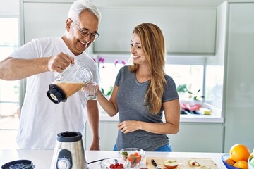 Middle age hispanic couple smiling happy pouring smoothie on glass at the kitchen.