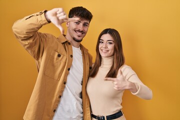 Fototapeta premium Young hispanic couple standing over yellow background smiling making frame with hands and fingers with happy face. creativity and photography concept.