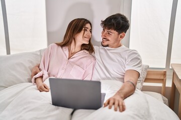 Mand and woman couple using laptop sitting on bed at bedroom