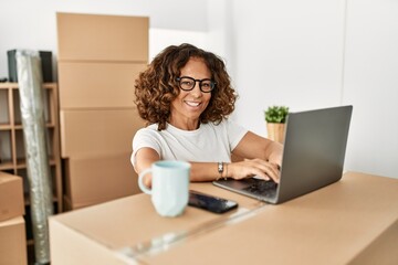 Middle age hispanic woman smiling confident using laptop at new home