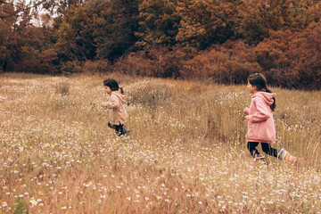 Two little girls in rubber boots and sweatshirts run and have fun against the background of the autumn forest