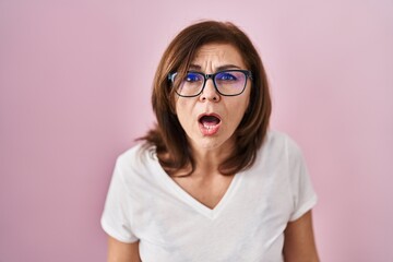 Middle age hispanic woman standing over pink background afraid and shocked with surprise and amazed...