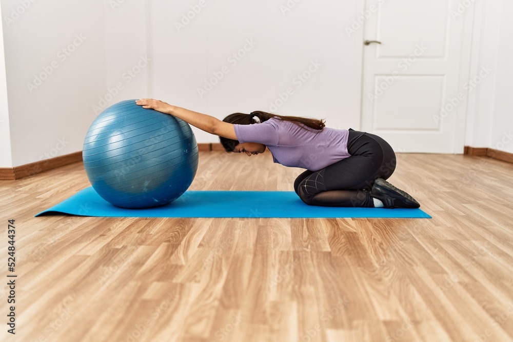 Sticker Young latin woman stretching using fit ball at sport center