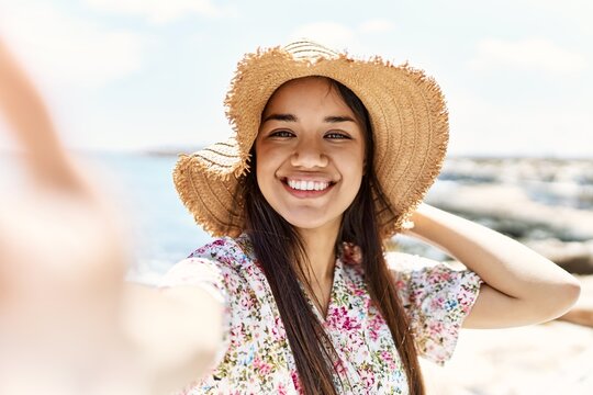 Young latin girl wearing summer hat making selfie by the camera at the beach.