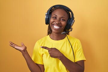 African american woman listening to music using headphones amazed and smiling to the camera while presenting with hand and pointing with finger.