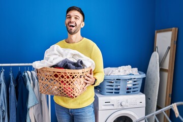 Hispanic man holding laundry basket smiling and laughing hard out loud because funny crazy joke.
