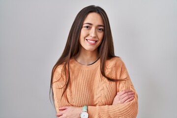 Young brunette woman standing over white background happy face smiling with crossed arms looking at the camera. positive person.