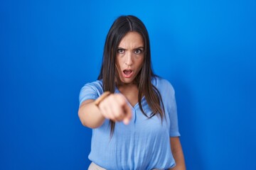 Fototapeta na wymiar Young brunette woman standing over blue background pointing displeased and frustrated to the camera, angry and furious with you