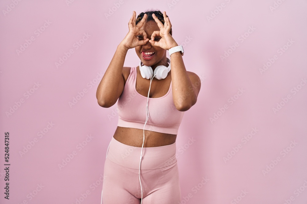 Sticker African american woman with braids wearing sportswear and headphones doing ok gesture like binoculars sticking tongue out, eyes looking through fingers. crazy expression.