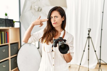 Beautiful caucasian woman working as photographer at photography studio shooting and killing oneself pointing hand and fingers to head like gun, suicide gesture.