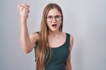 Fototapeta na wymiar Young caucasian woman standing over white background angry and mad raising fist frustrated and furious while shouting with anger. rage and aggressive concept.