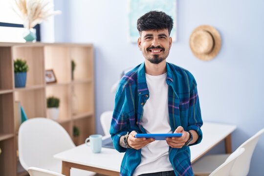 Young hispanic man using touchpad sitting on table at home