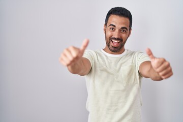 Fototapeta premium Hispanic man with beard standing over isolated background approving doing positive gesture with hand, thumbs up smiling and happy for success. winner gesture.