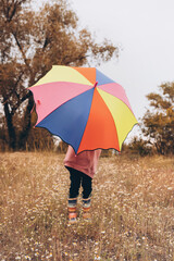 little girls in rubber boots and a sweatshirt covered themselves with a colorful umbrella, autumn orange background and meadow