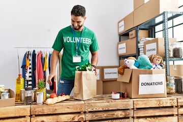 Young arab man wearing volunteer uniform preparing groceries paper bag at charity center