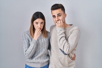 Young hispanic couple standing over white background looking stressed and nervous with hands on mouth biting nails. anxiety problem.
