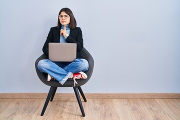 Young hispanic woman sitting on chair using computer laptop thinking concentrated about doubt with...