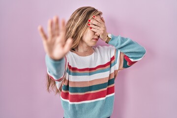 Young blonde woman standing over pink background covering eyes with hands and doing stop gesture with sad and fear expression. embarrassed and negative concept.