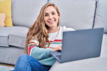 Young blonde woman using laptop sitting on floor at home