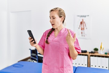 Young caucasian woman wearing physiotherapist uniform having video call at physiotherapy clinic